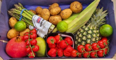 Seasonal fruit and veg box, with potatoes, asparagus, strawberries, pineapple and tomatoes on the vine.